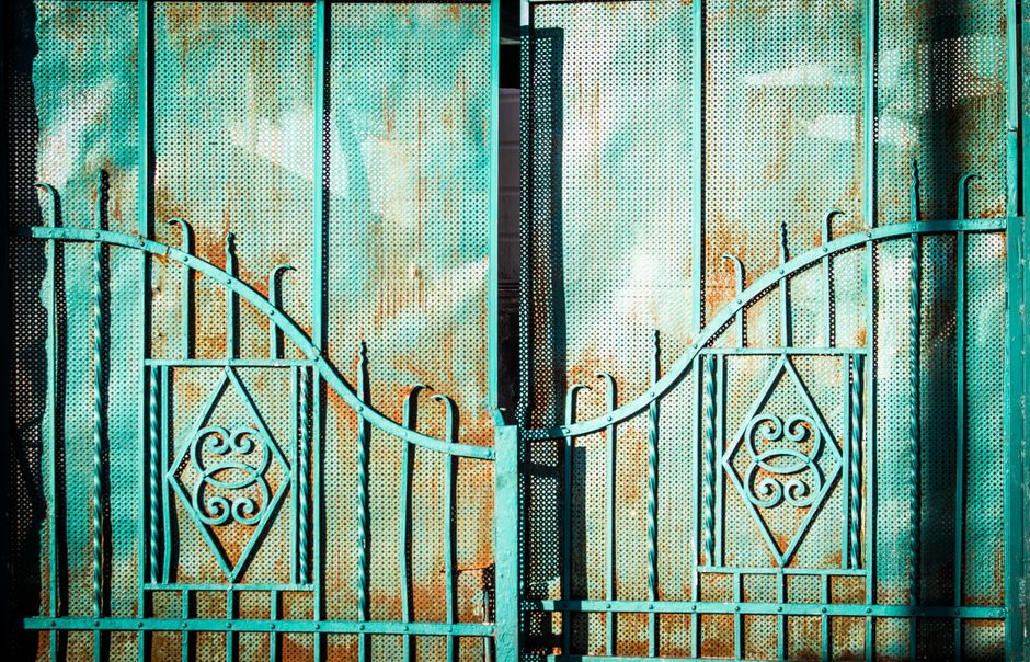 A black metal gate with decorative pickets set in a fence line.