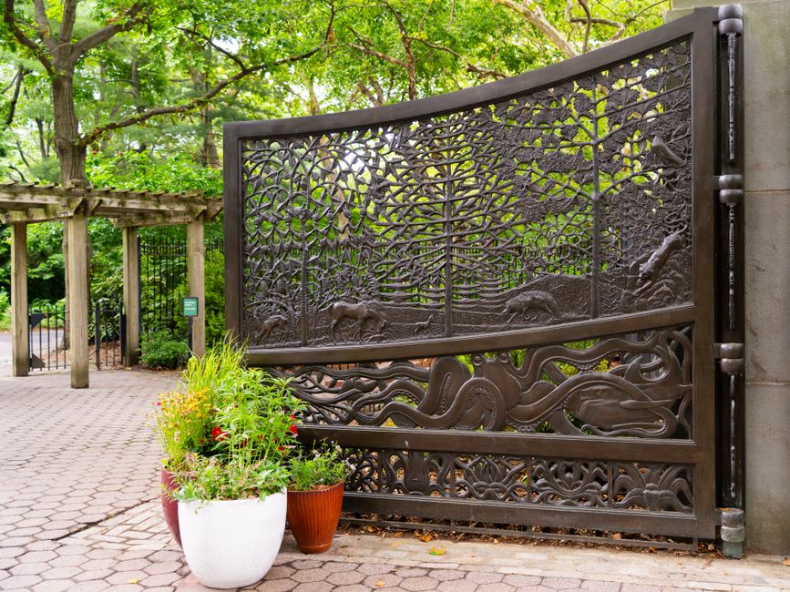 A black metal gate with decorative pickets set in a fence line.